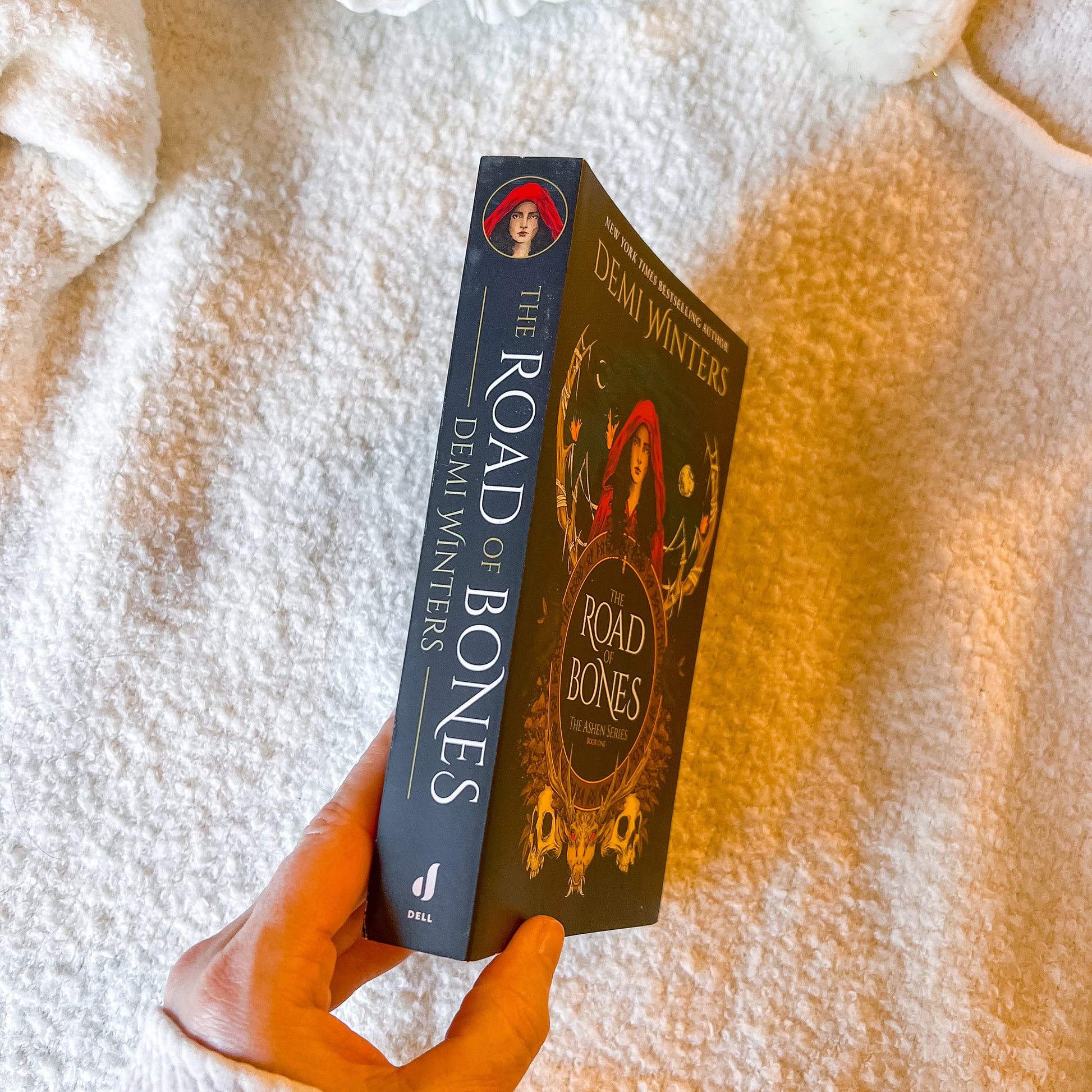 Book titled 'The Road of Bones' by Demi Winters held against a textured white and orange background.