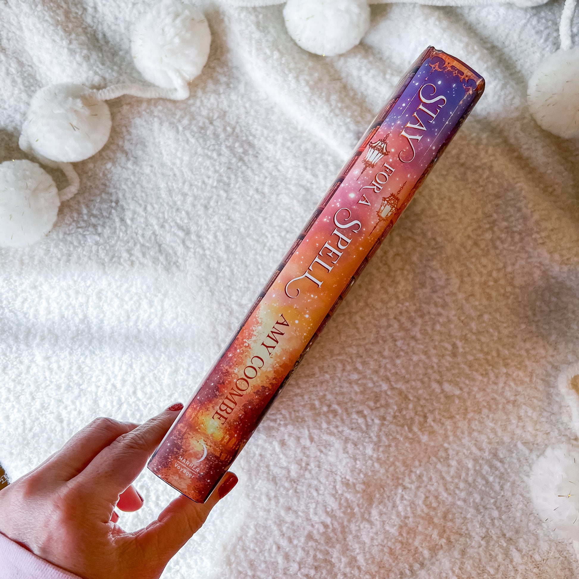 book spine for Stay a Spell with gradient design held by a hand on a textured white background