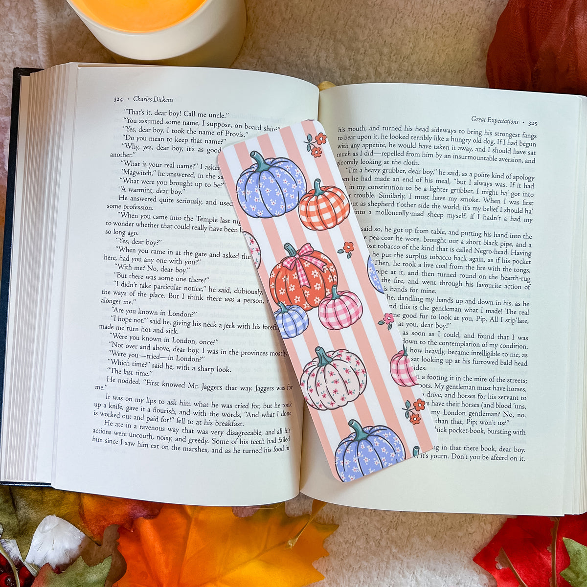 A bookmark with a pumpkin-themed design, styled on an open book with a warm blanket background.