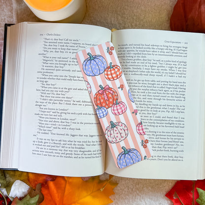A bookmark with a pumpkin-themed design, styled on an open book with a warm blanket background.