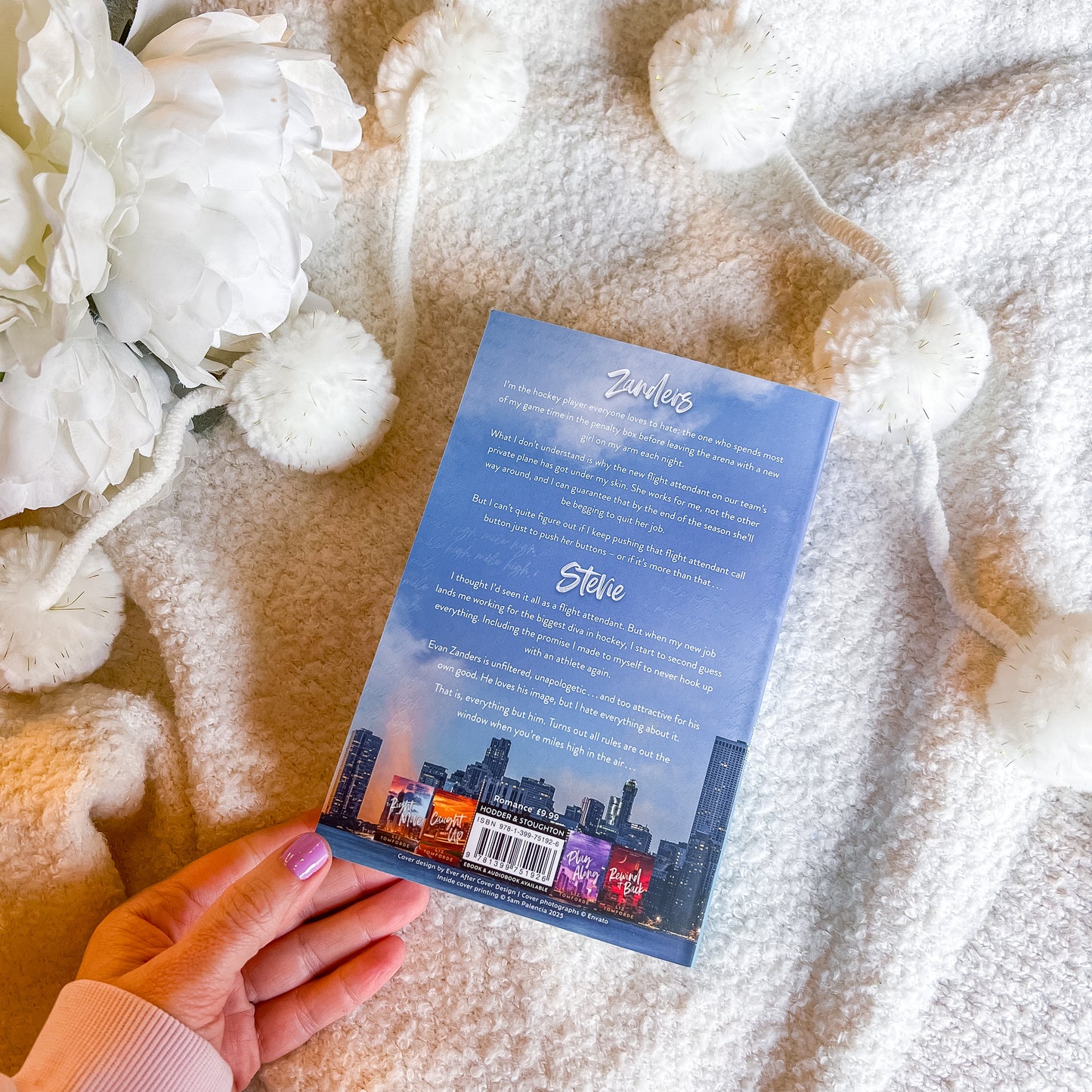 Book back cover held by a hand on a textured surface with white flowers