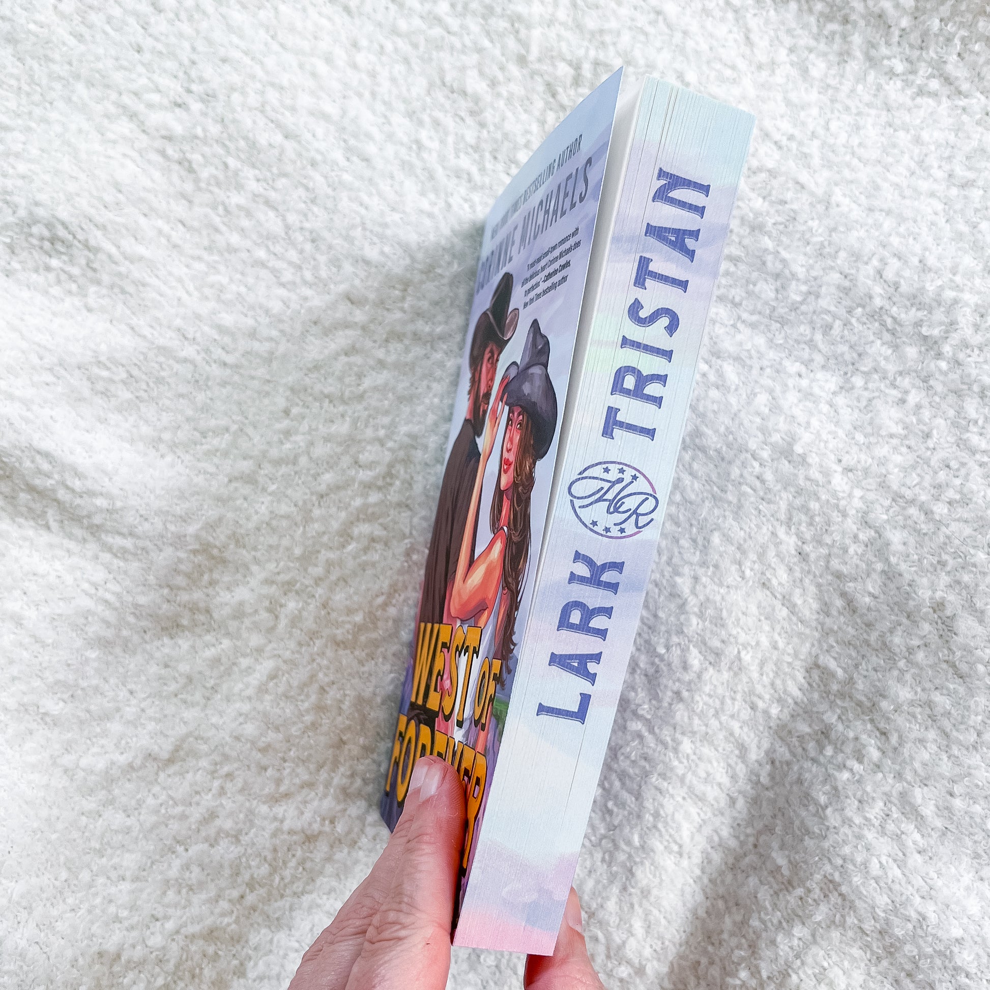 Book titled 'West of Forever' by Lark Tristan held against a textured white background