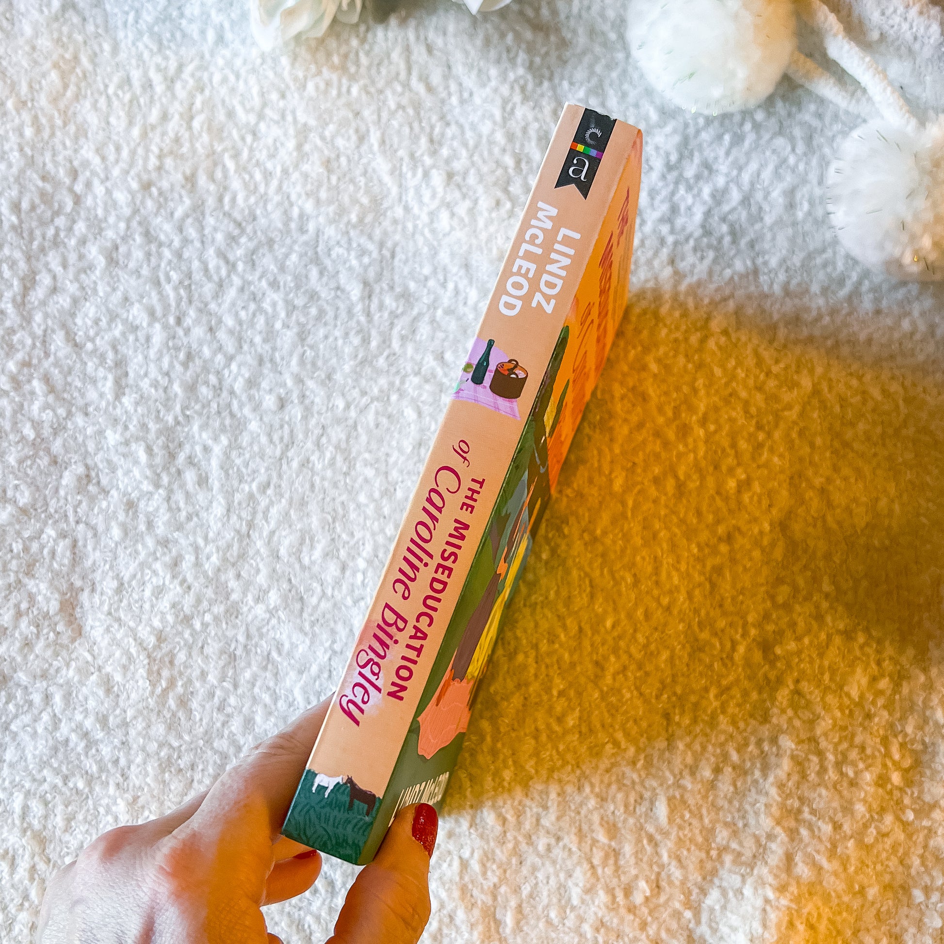 The book "the miseducation of carolin bingley" on a pale pink background