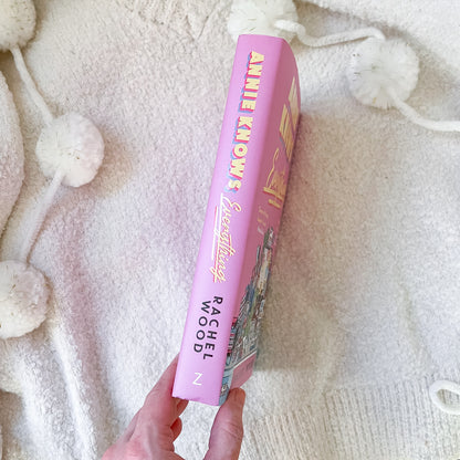 Pink book titled 'Annie Knows' held against a textured white background