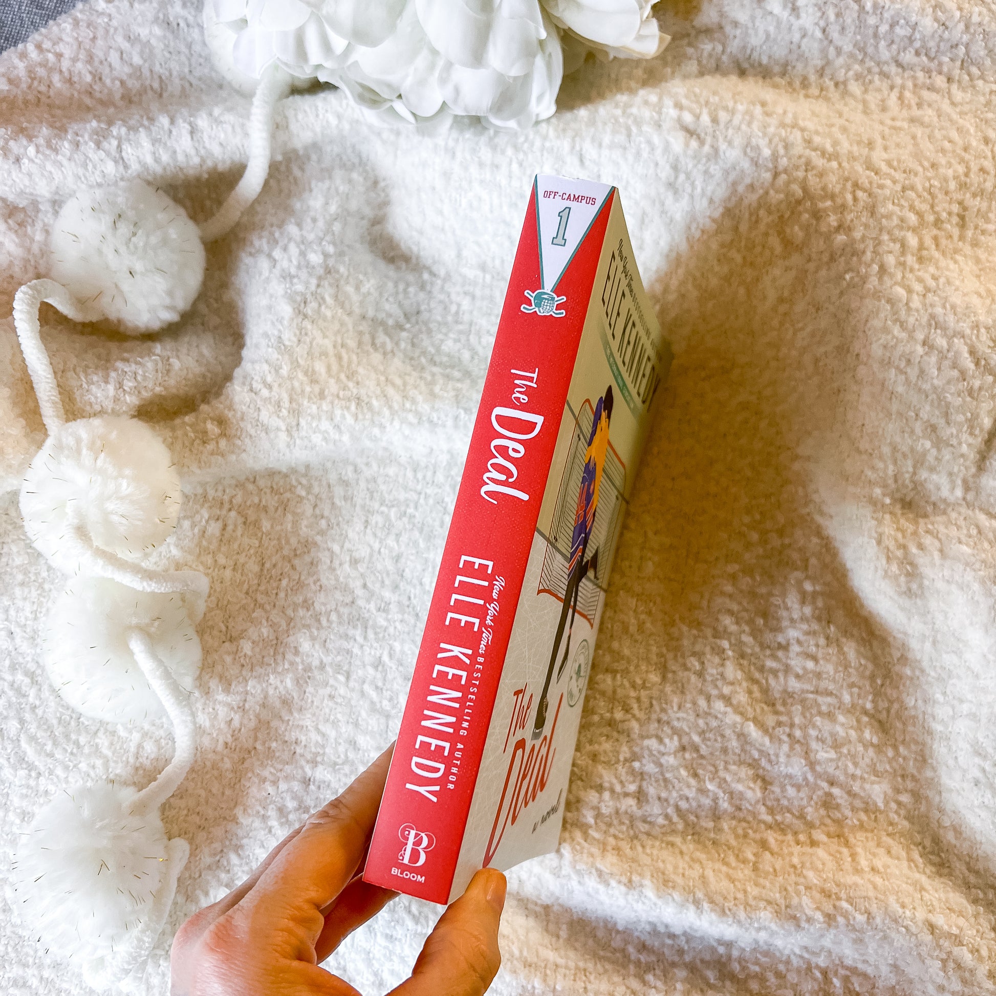 Book titled 'The Deal' by Ellie Kenneedy held against a soft, textured white background