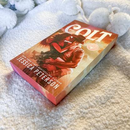 A boxed copy of the book 'Colt' by Jessica Peterson, featuring a romantic western cover illustration, placed on a soft cream-colored textured blanket.