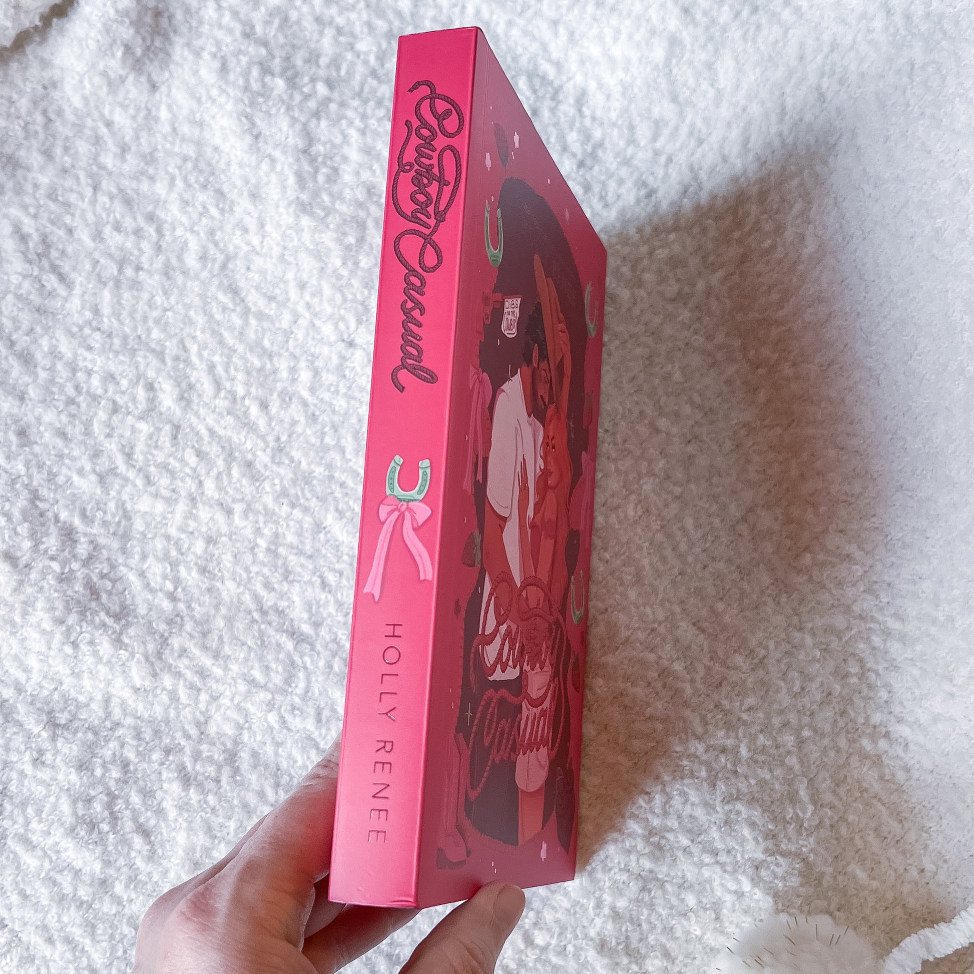 Pink book with 'Holly Renee' branding held by a hand on a white textured surface