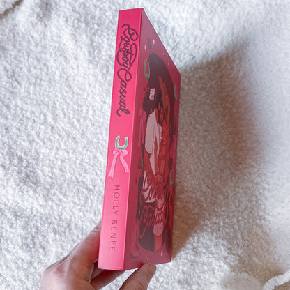 Pink book with 'Holly Renee' branding held by a hand on a white textured surface