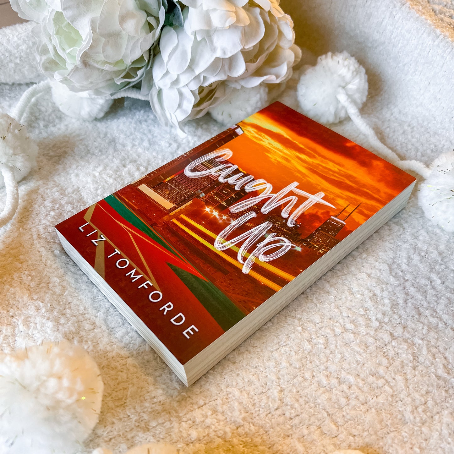 Book titled 'Caught Up' by Liz Tomforde on a soft surface with flowers.