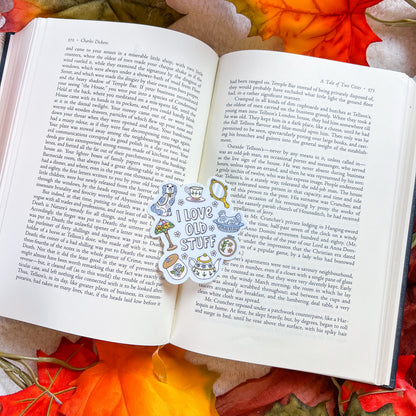 A die-cut sticker sheet featuring vintage-style illustrations and text, including a cat wearing sunglasses and the phrase 'I LOVE OLD STUFF', displayed on the pages of an open book with autumn leaves in the background.