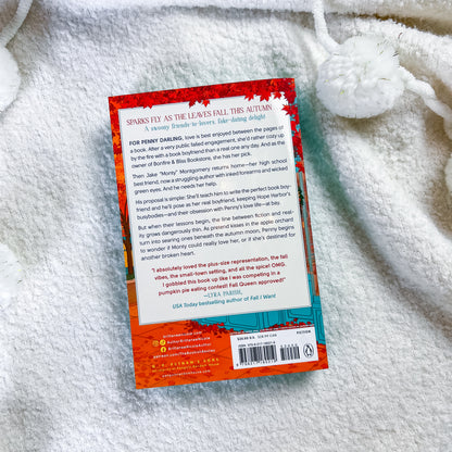 The back cover of the paperback book photographed flat on a white textured blanket. The cover features a vibrant red and orange fiery design on the top half and a teal blue section on the bottom right containing the barcode and author details.
