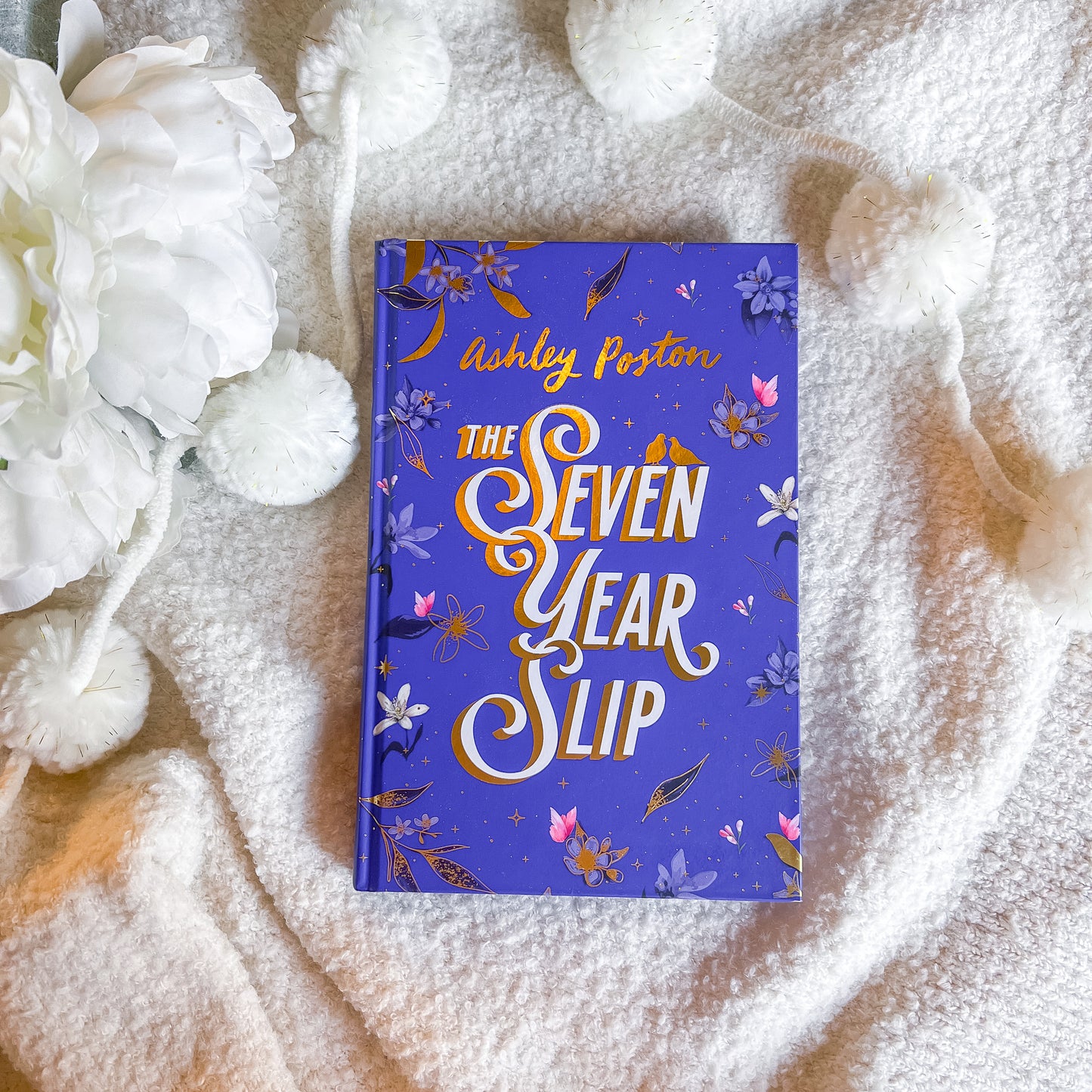 Book titled 'The Seven Year Slip' by Ashley Poston on a textured surface with white flowers.