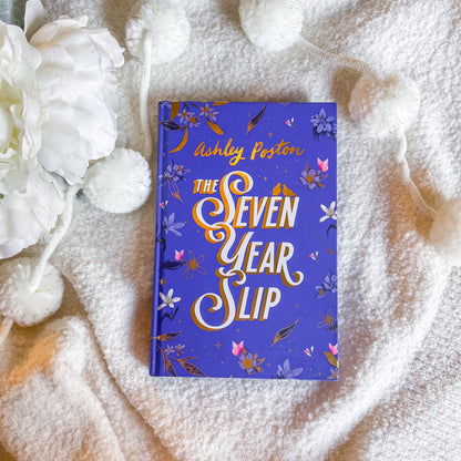 Book titled 'The Seven Year Slip' by Ashley Poston on a textured surface with white flowers.
