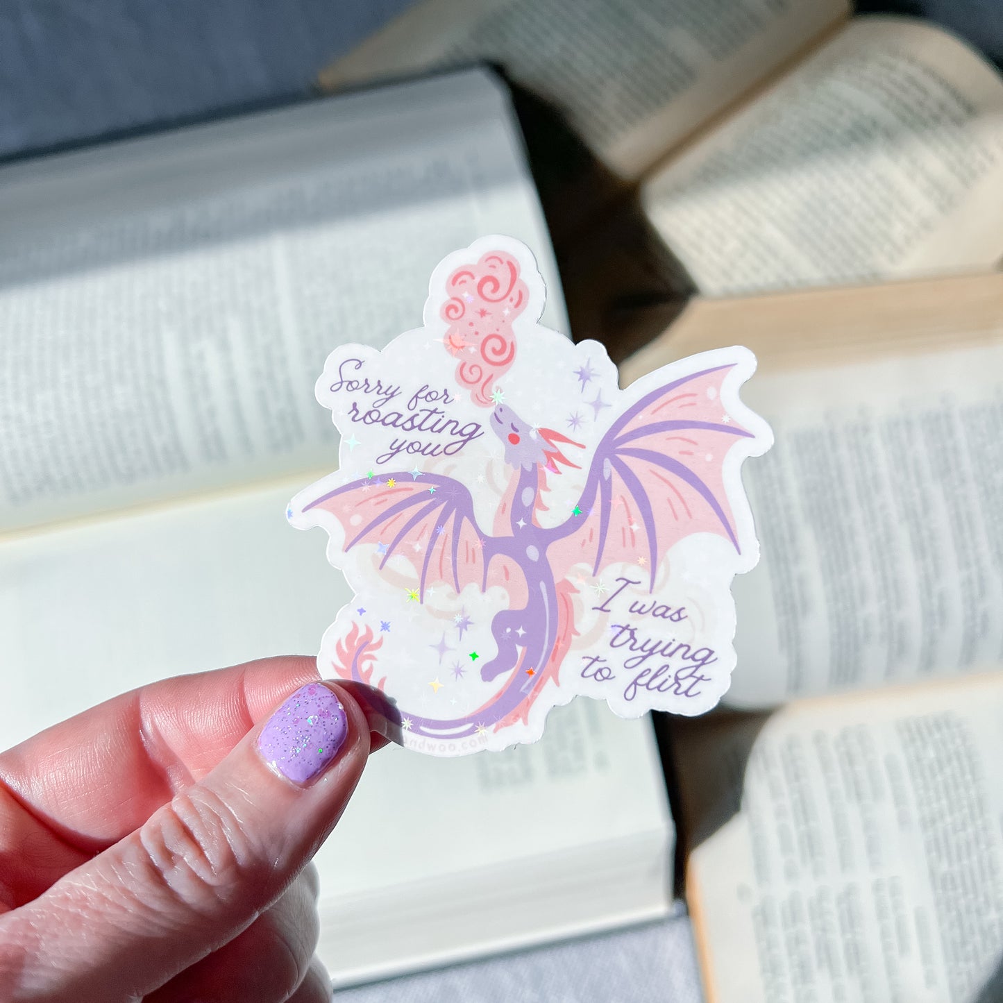 Hand holding a dragon-shaped sticker with text on an open book background