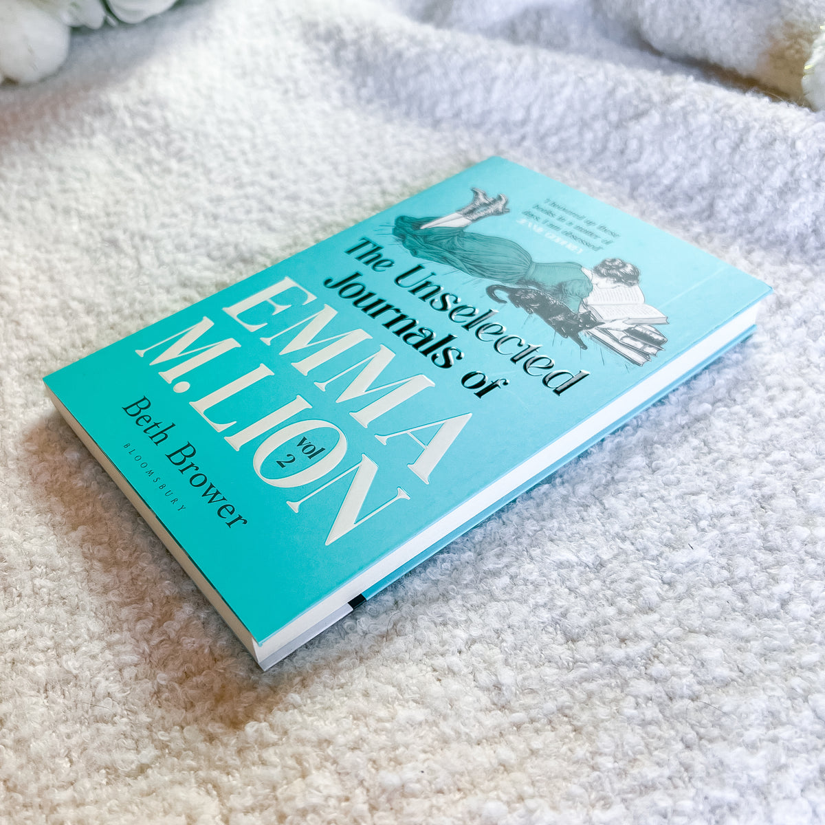 The Unselected Journals of Emma, Volume 3 by Beth Brower, a hardcover book with a turquoise cover, resting on a textured white blanket.