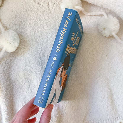Book titled 'The Love Hypothesis' by Ali Hazelwood held against a soft white background