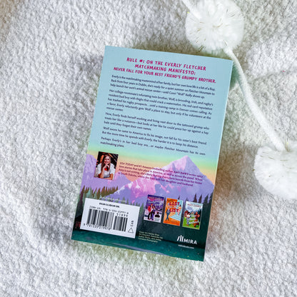 The back cover of the book, placed on a white textured blanket. The cover features a light blue top section with black text, a colorful rainbow gradient middle section, and a dark teal bottom section with a barcode and character illustrations.