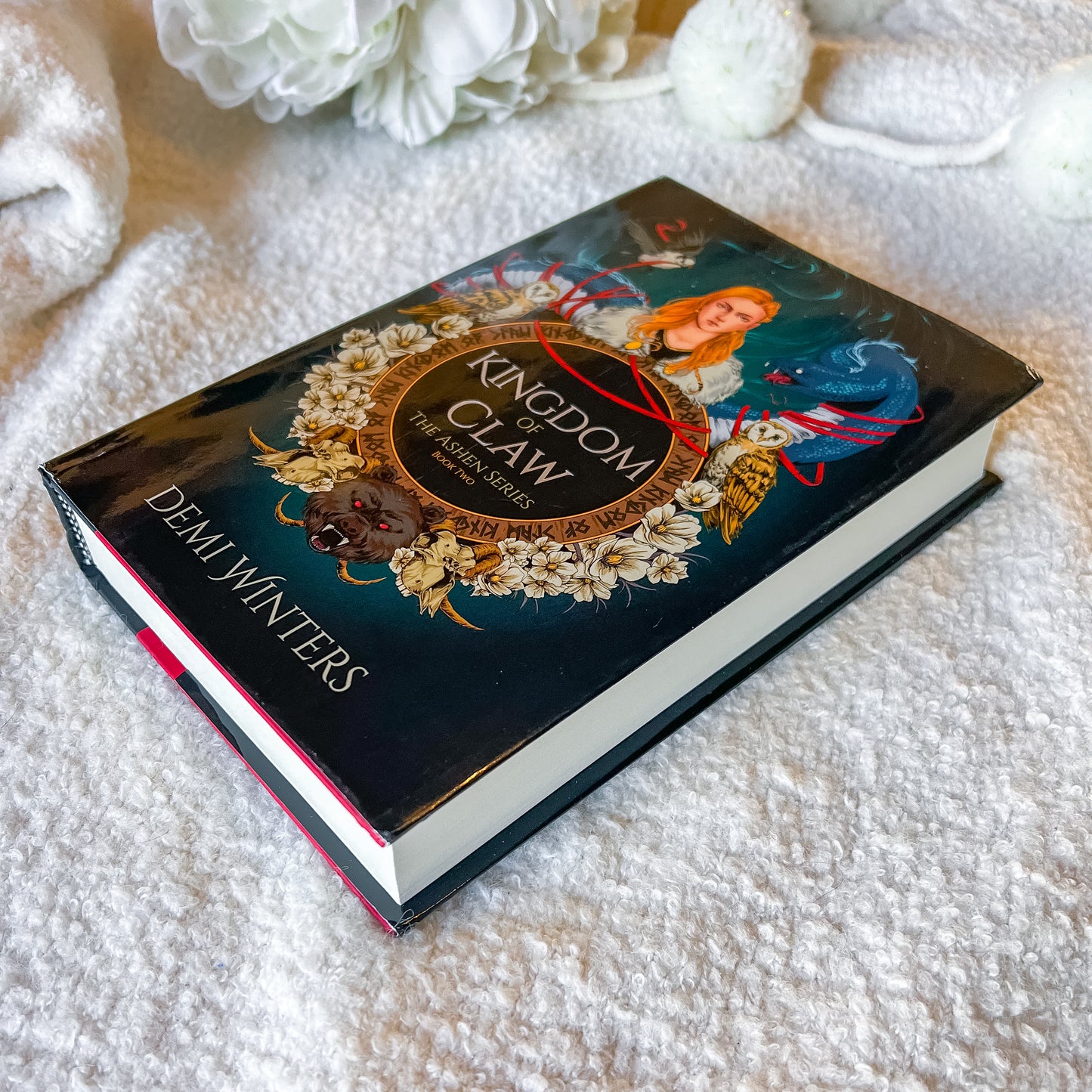 Book titled 'Kingdom of Claws' by Demi Winters on a textured surface with flowers in the background