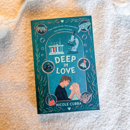The book cover of 'Deep in Love' by Nicole Cubba, featuring a teal and blue marine-themed illustration with a couple at the bottom, photographed flat on a textured cream-colored blanket.
