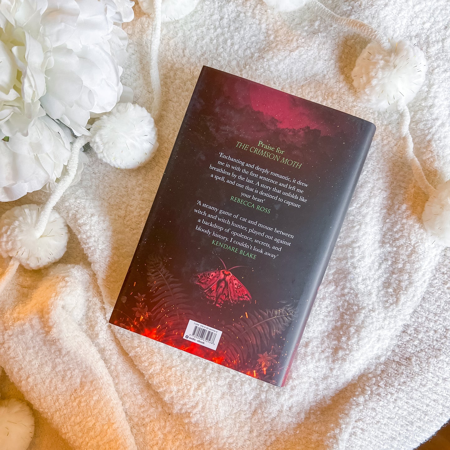 Book with a red and black cover on a textured surface with white flowers.