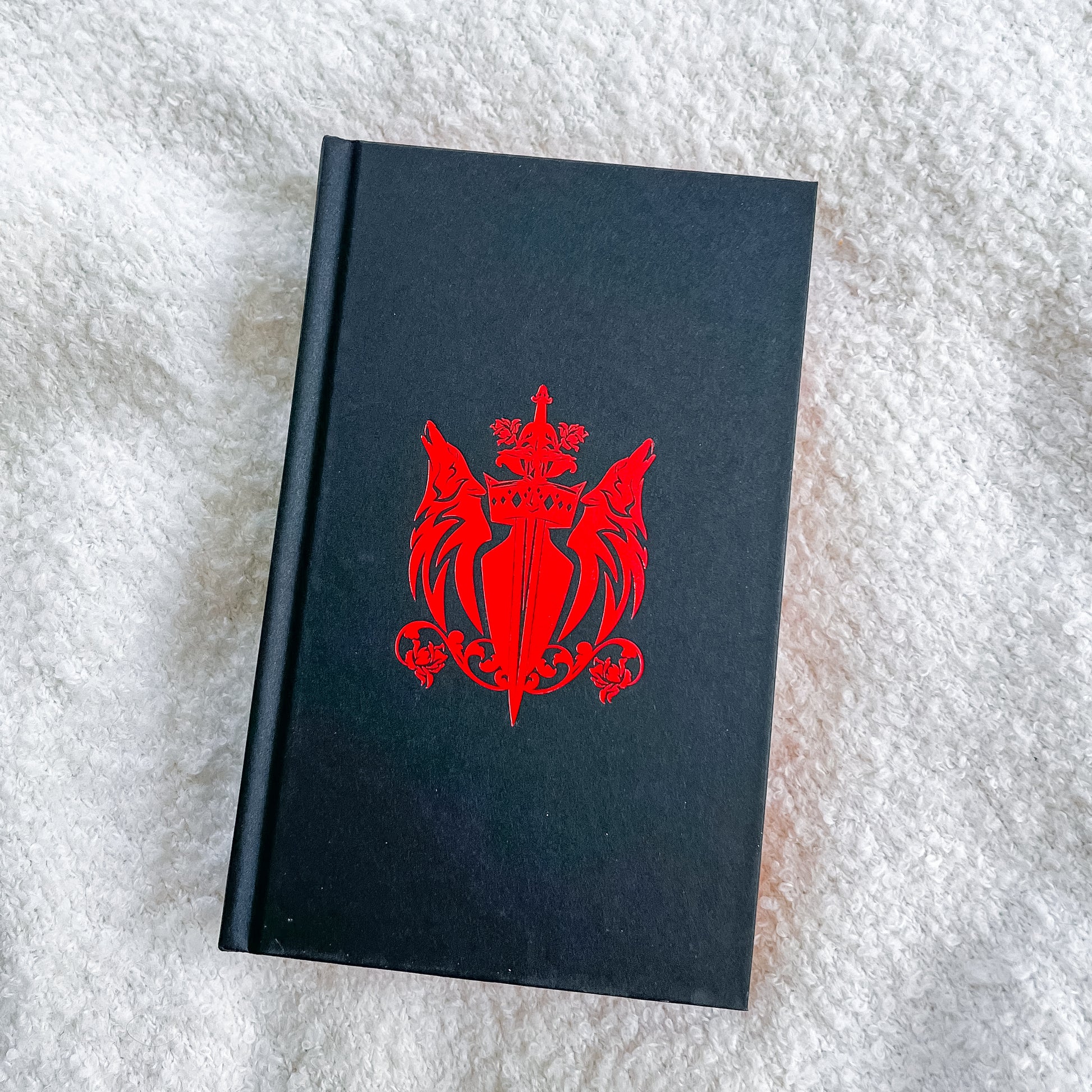 Black book with a red emblem on a textured white surface