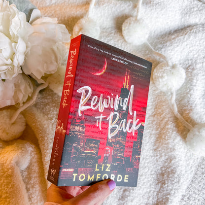 Book titled 'Rewind It Back' by Liz Tomforde held against a soft, textured background with flowers.