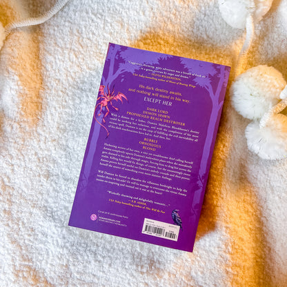 The back cover of a purple book styled flat-lay on a textured white blanket with decorative white pom-poms.
