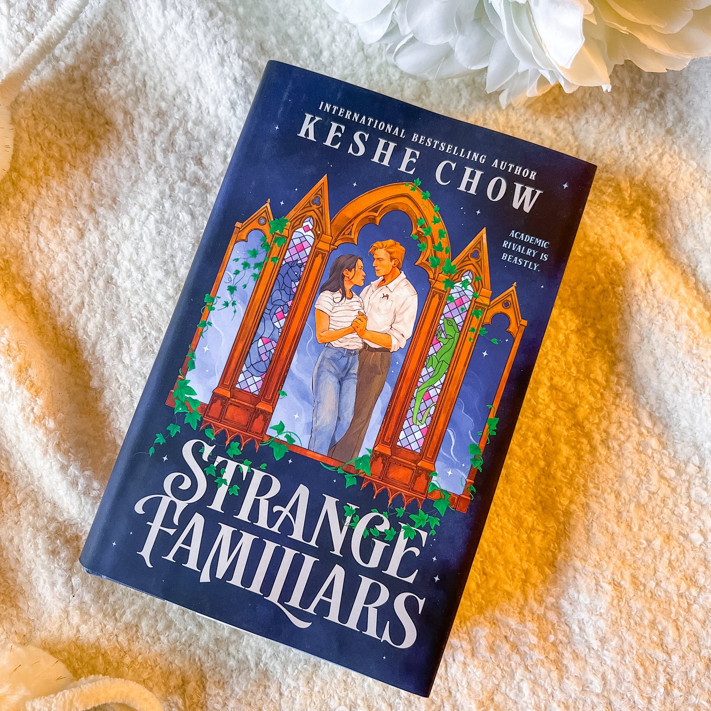 Book titled 'Strange Familiars' by Keshe Chow on a textured surface with flowers.