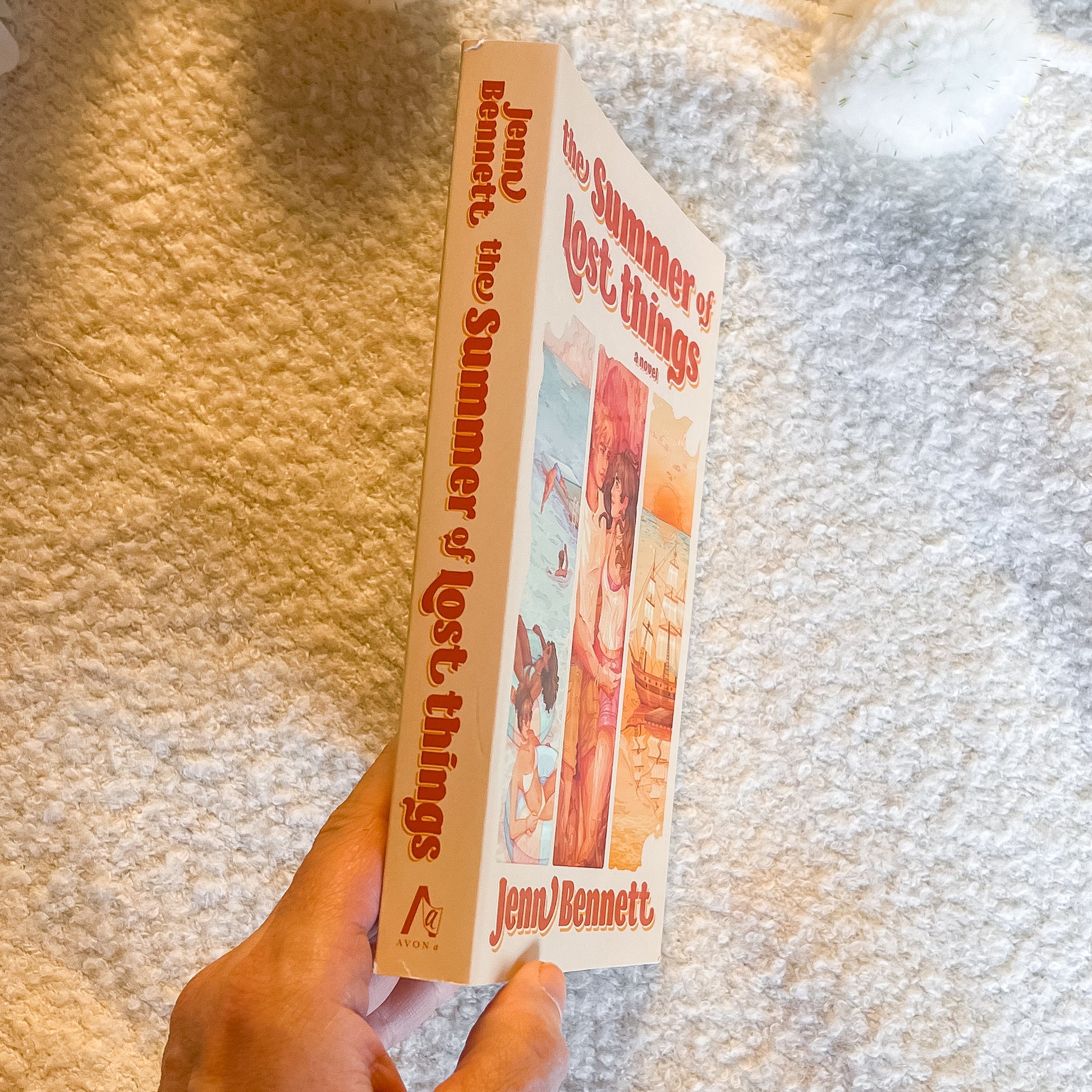 Book titled 'The Summer of Lost Things' by Jenn Bennett held against a textured surface.