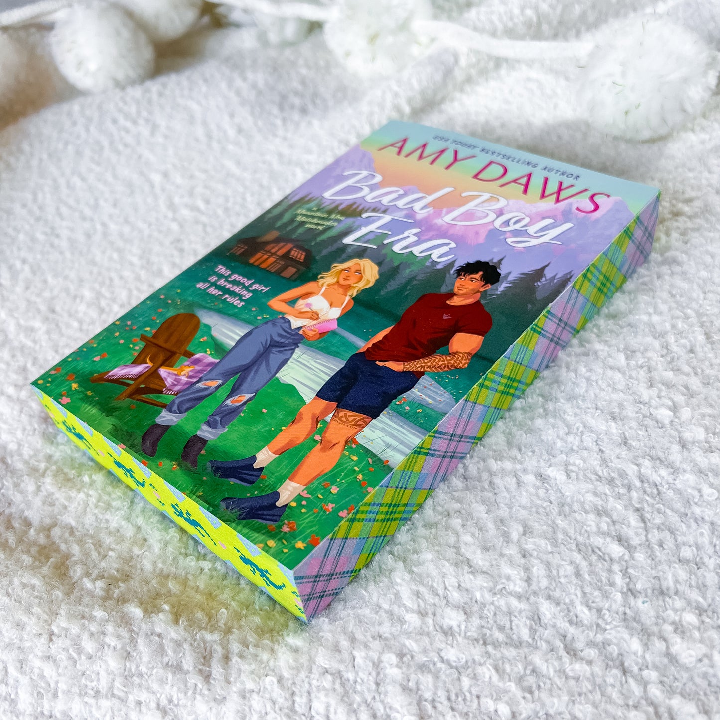 A boxed book titled "Bad Boy Era" by Amy Daw's, featuring colorful illustrated cover art and a plaid-patterned box, placed on a soft white textured blanket.