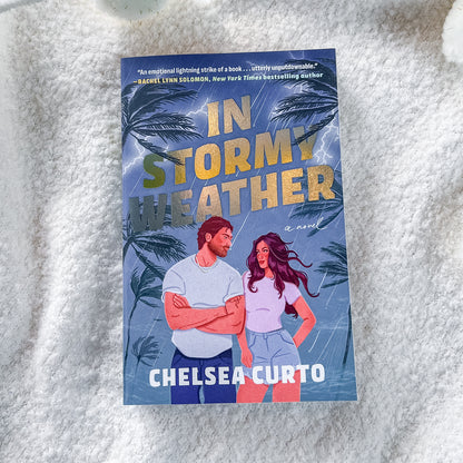 The book cover of 'In Stormy Weather' by Chelsea Curto, featuring a blue tropical storm background with palm trees and an illustration of a man and woman, placed on a white textured blanket.