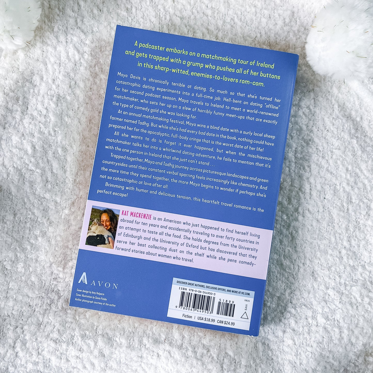 The back cover of a blue book, photographed flat on a white textured faux fur surface. The cover features a dark blue background with white text, a small author portrait, and a barcode at the bottom.