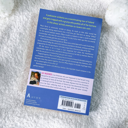 The back cover of a blue book, photographed flat on a white textured faux fur surface. The cover features a dark blue background with white text, a small author portrait, and a barcode at the bottom.