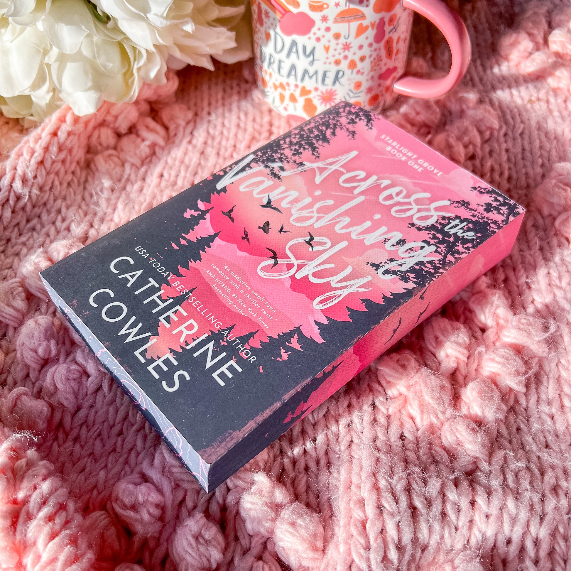 Book titled 'Across the Vanishing Sky' by Catherine Cowles on a pink textured surface with flowers and a mug.