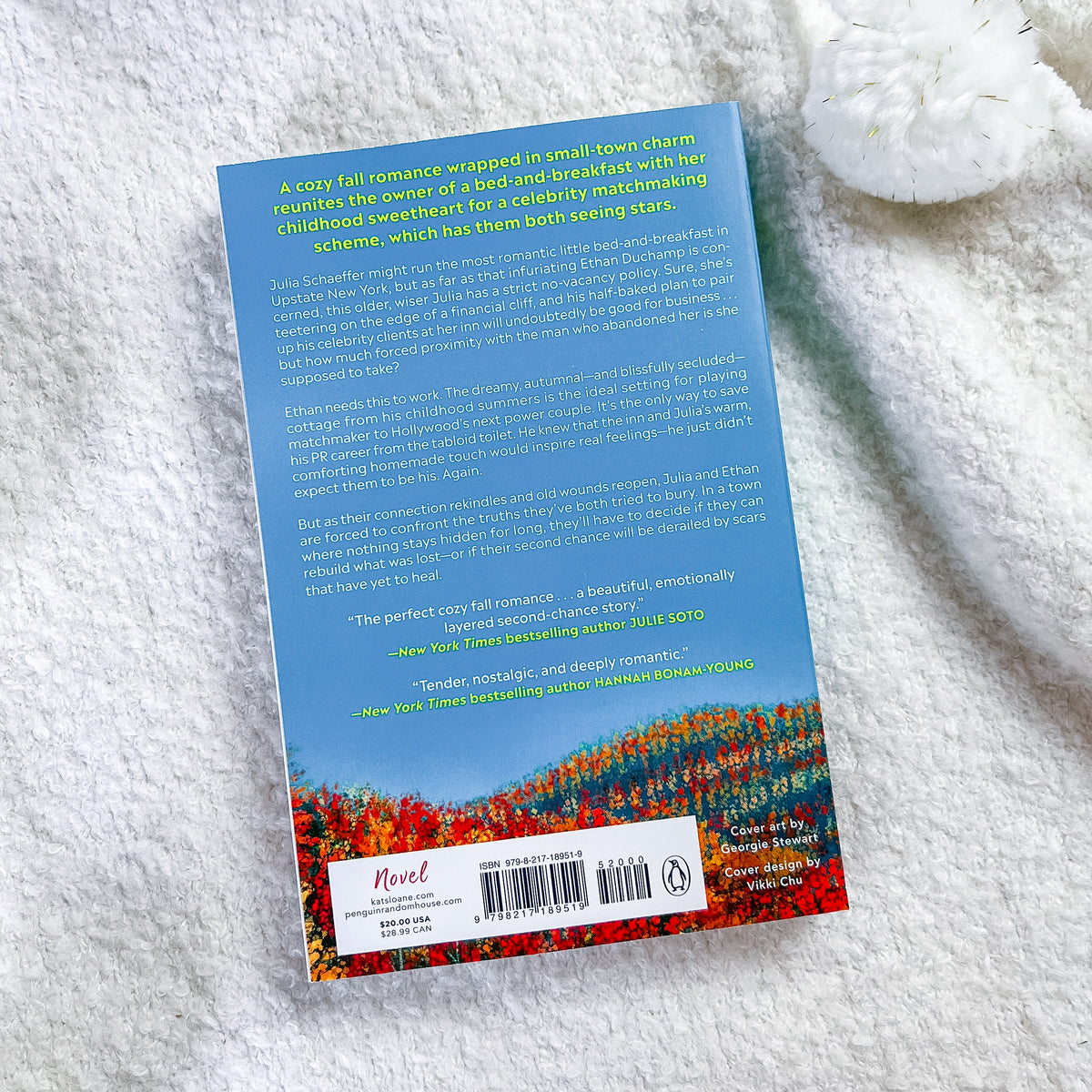 The back cover of a book, displayed on a white textured fabric background. The cover features a blue background with a colorful field of red, orange, and yellow flowers at the bottom, along with a white publisher label for Penguin Random House.