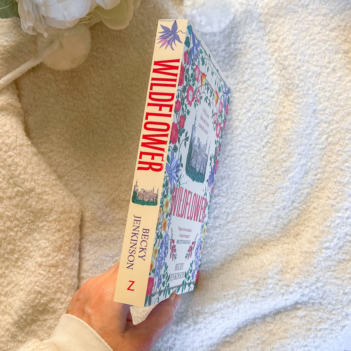 Book titled 'Wildflower' held by a hand on a soft fabric background