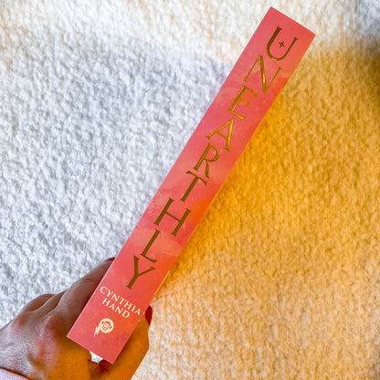 Book titled 'Unearthly' by Cynthia Hand held against a textured white and yellow background