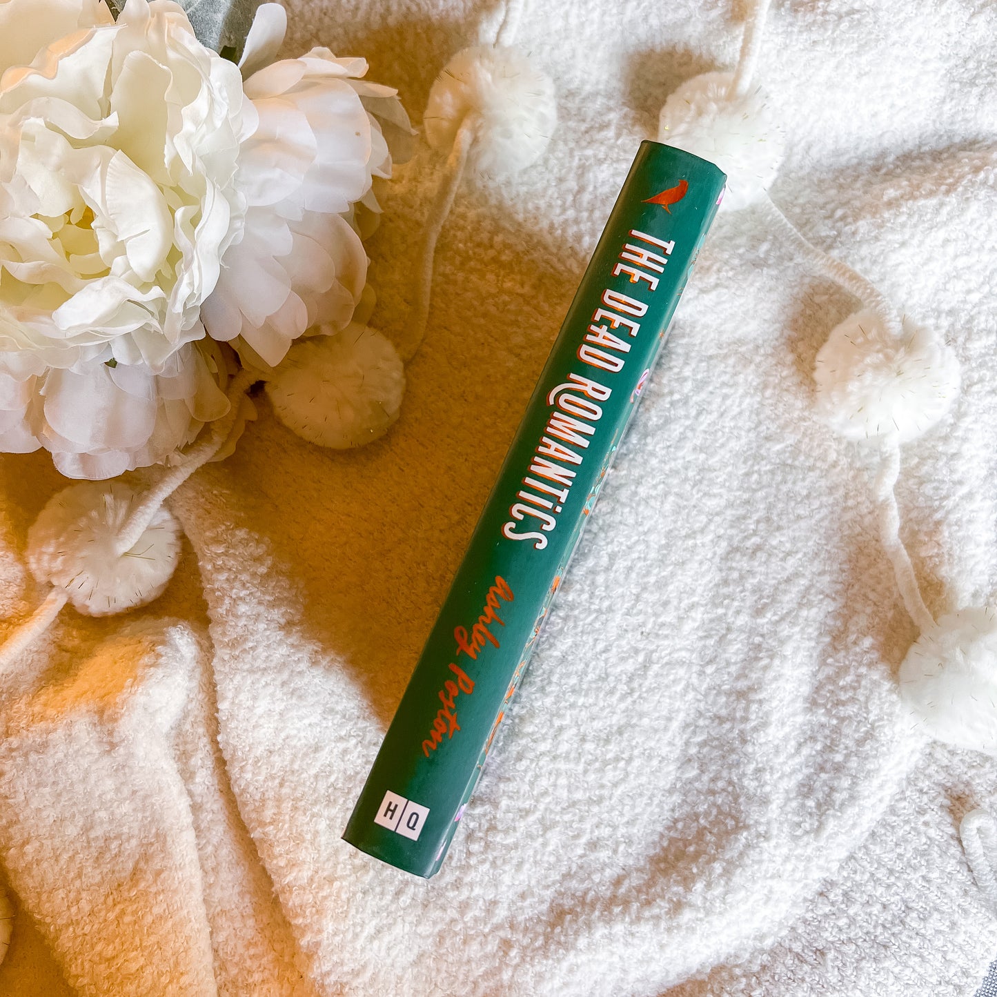 Book titled 'The Dead Romantics' on a textured surface with white flowers.