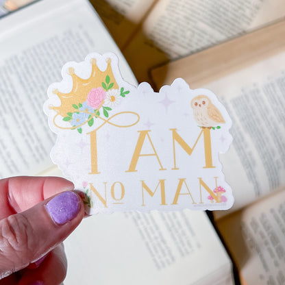 Sticker with 'I AM NO MAN' text held by a hand over an open book.
