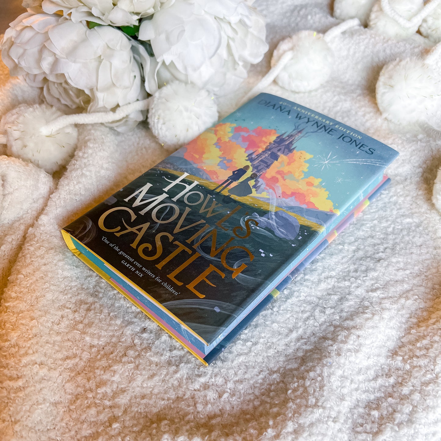 Book titled 'Howl's Moving Castle' by Diana Wynne Jones on a textured surface with flowers.