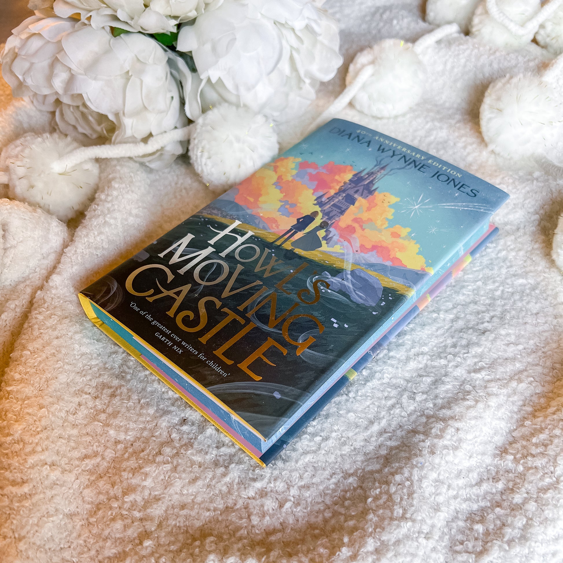 Book titled 'Howl's Moving Castle' by Diana Wynne Jones on a textured surface with flowers.