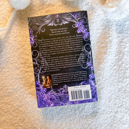 The back cover of the book by Smith, featuring a dark purple and black background with ornate silver swirls, purple berries, and a small illustration of a woman, laid flat on a textured cream-colored blanket.