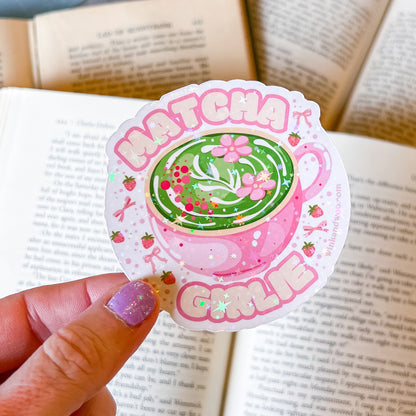 Sticker with a green tea cup design and 'Matcha Girl' text held over an open book.