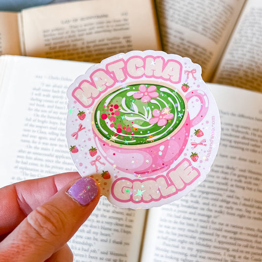 Sticker with a green tea cup design and 'Matcha Girl' text held over an open book.