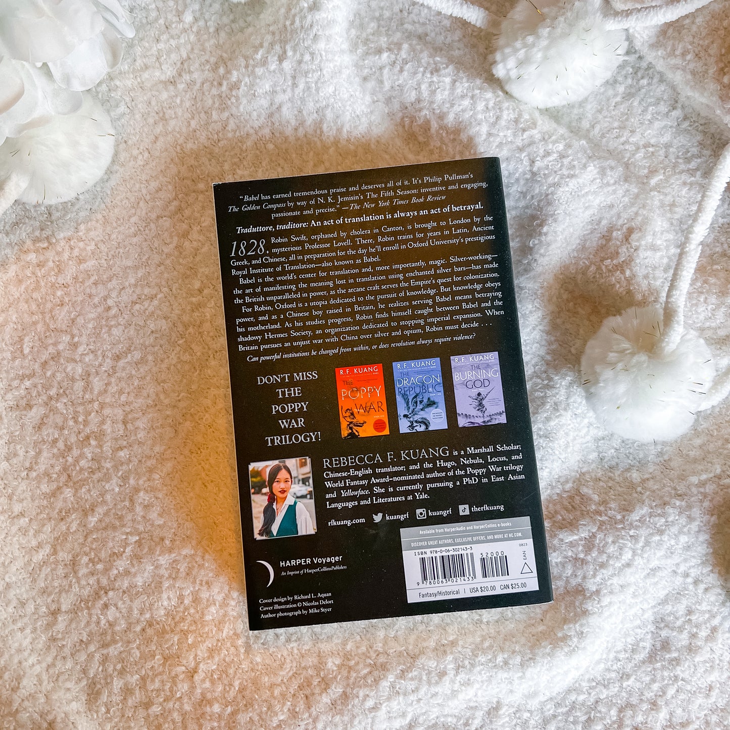 The back cover of a book, displayed flat on a soft white textured blanket with decorative white flowers in the corners.
