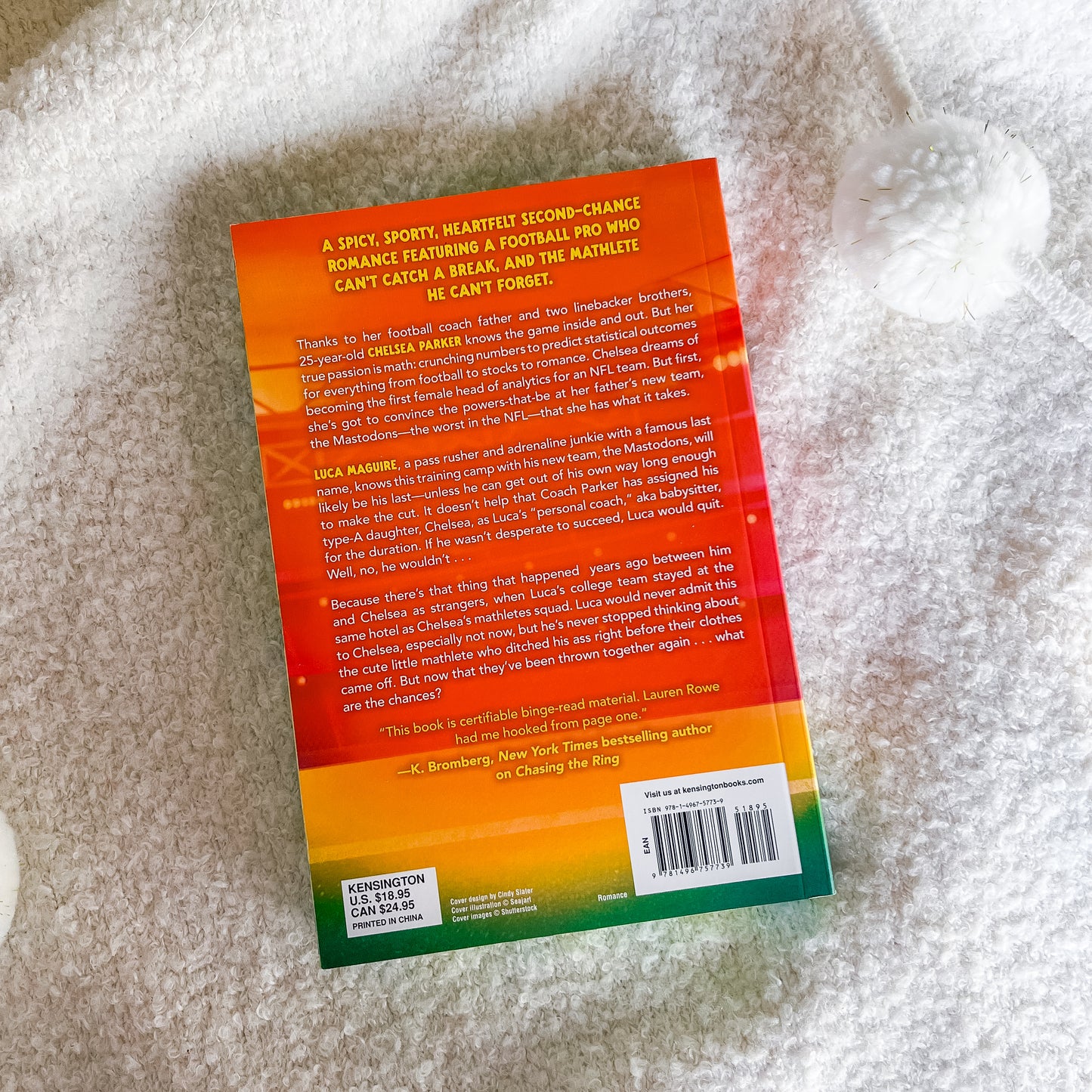 The back cover of the book, featuring a vibrant orange-to-yellow-to-green gradient design with text and a barcode, photographed on a white textured blanket.
