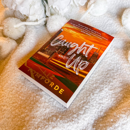 Book titled 'Caught Up' by Liz Forde on a textured surface with flowers.