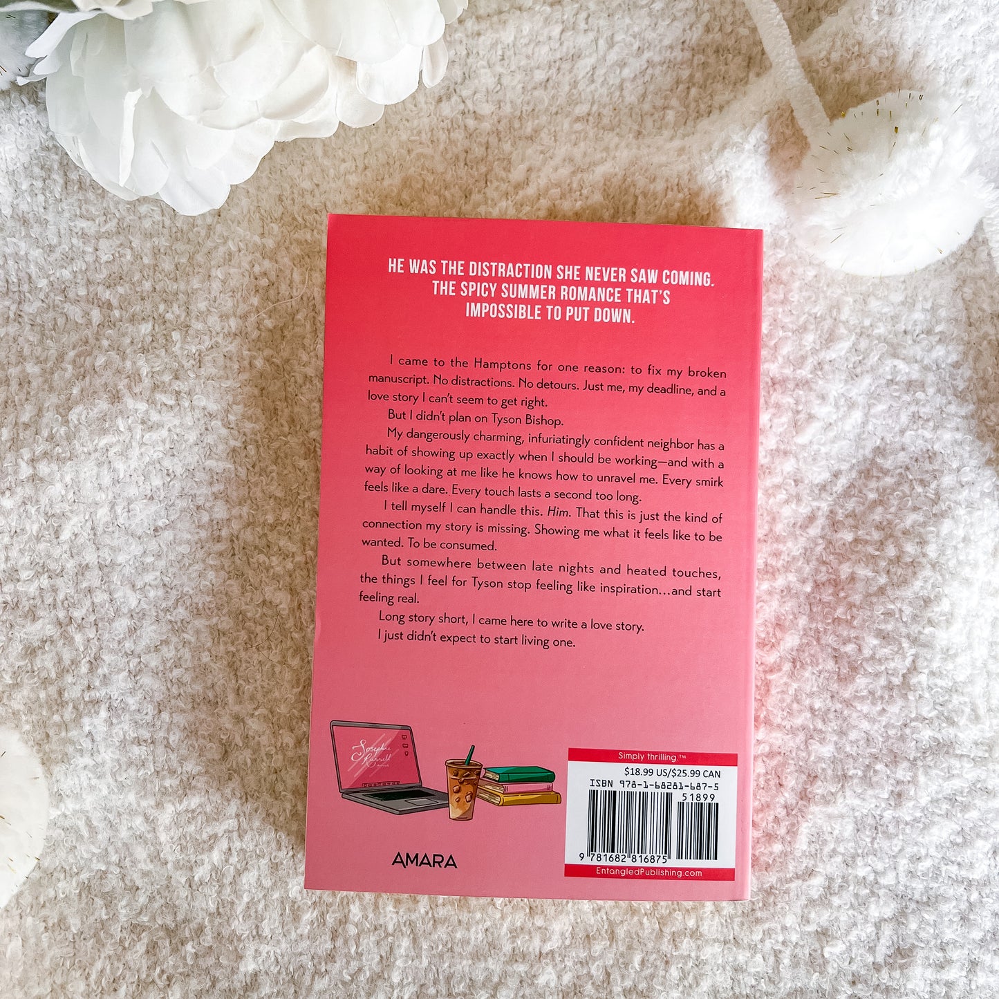 The back cover of a pink book by Amara, styled on a textured white fabric background with a white flower in the corner.