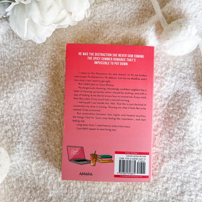 The back cover of a pink book by Amara, styled on a textured white fabric background with a white flower in the corner.