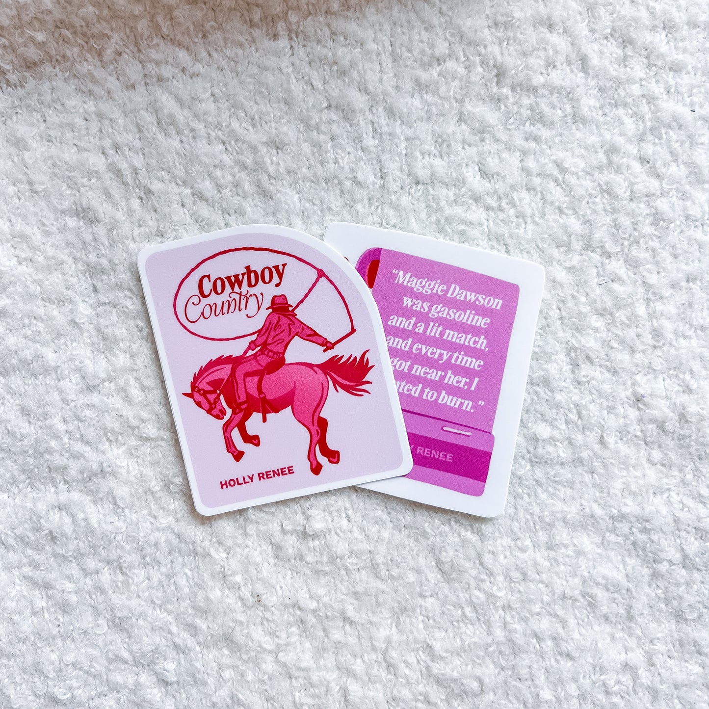 Two printed stickers laid on a white textured fabric background. One card shows a pink cowboy riding a horse with the words 'Cowboy Country' and 'HOLLY RENEE.
